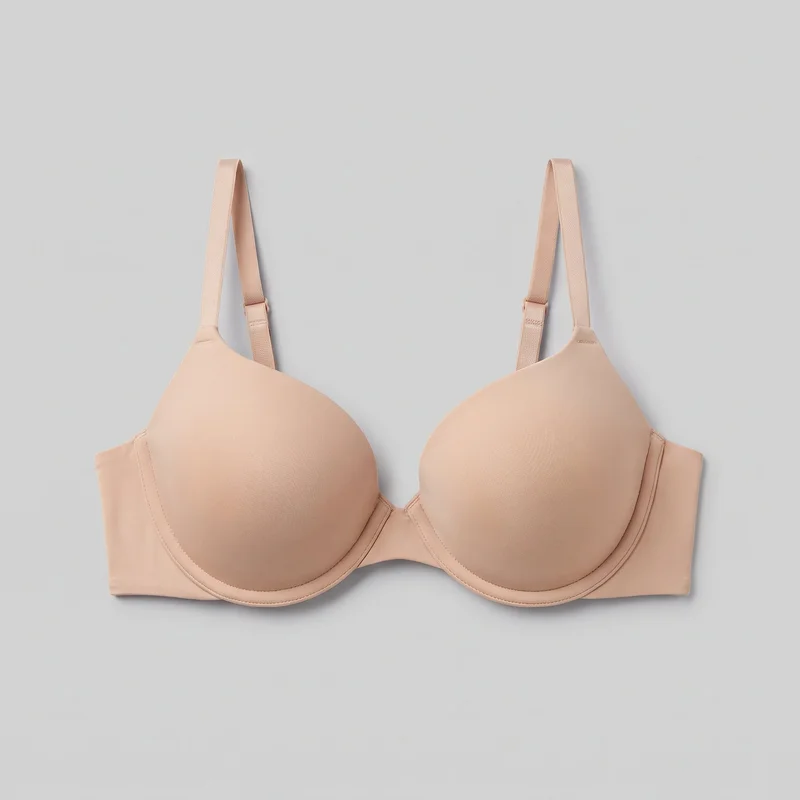 A nude molded underwire T-shirt bra is shown in a standalone front view. It has two smooth seamless contoured cups, a low center gore, underwire channels along the lower cup edges, straight side wings, visible stitching at the cup edges and strap attachment points, and narrow adjustable shoulder straps with slide adjusters. The back closure is not shown, and no logos or embellishments are visible.