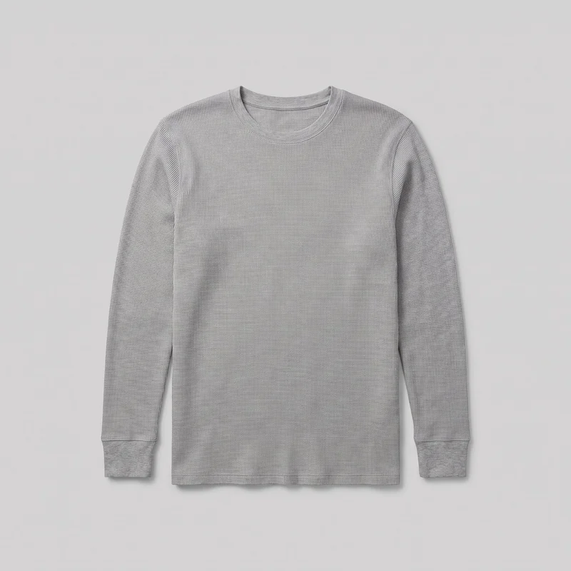 A grey men's thermal base-layer shirt is shown flat in a full front view. It has long sleeves, a regular straight silhouette, set-in shoulders, a ribbed crew neck and sleeve cuffs, visible shoulder seams, and a straight full-length hem. Fine waffle-knit texture covers the body and sleeves, with clean stitched edges and no visible logos, prints, patches, embroidery, or embellishments.