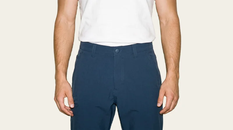 Men's navy hiking trousers shown from the front, framed at the hips with the hips level. The trousers are displayed against a flat alabaster backdrop.