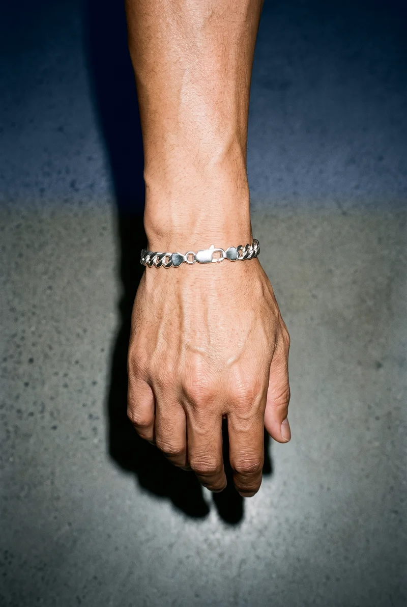 A man's hand and wrist are shown from above with the knuckles facing forward, wearing a silver chain bracelet. The powder-blue studio wall forms the backdrop.