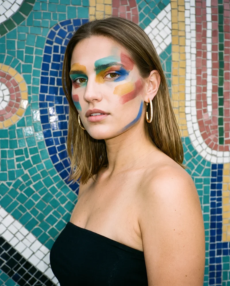 A 21-year-old Slavic woman is shown in a bust-length frame from a front three-quarter angle, wearing gold ear cuffs. Her shoulders are square and her expression is neutral. A Barcelona Modernist Building serves as the backdrop.