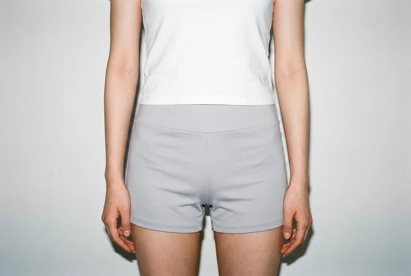 Women's grey gym shorts shown from the front, framed from the hips with the hips level. A cloud-white studio wall forms the backdrop.