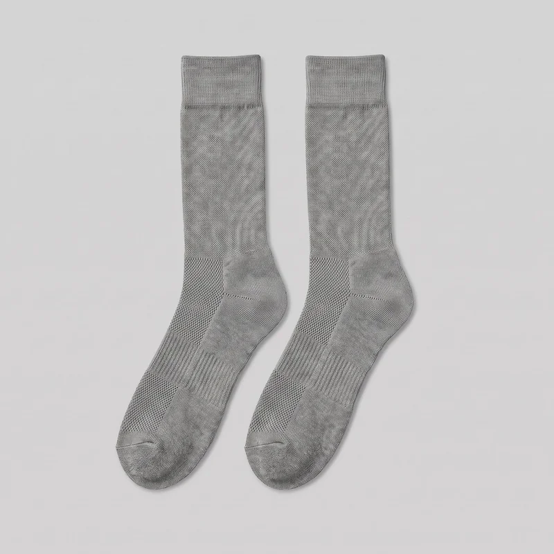 A complete pair of grey crew-length performance socks is shown flat, with the cuffs, tubular legs, shaped heel pockets, soles, and rounded toes visible. The socks have straight ribbed cuffs, an allover fine textured knit, denser contrast-knit zones at the cuffs, heels, toes, and soles, and visible panel transitions around the heel, instep, arch, and toe seams. No logos, prints, patches, embroidery, or embellishments are visible.