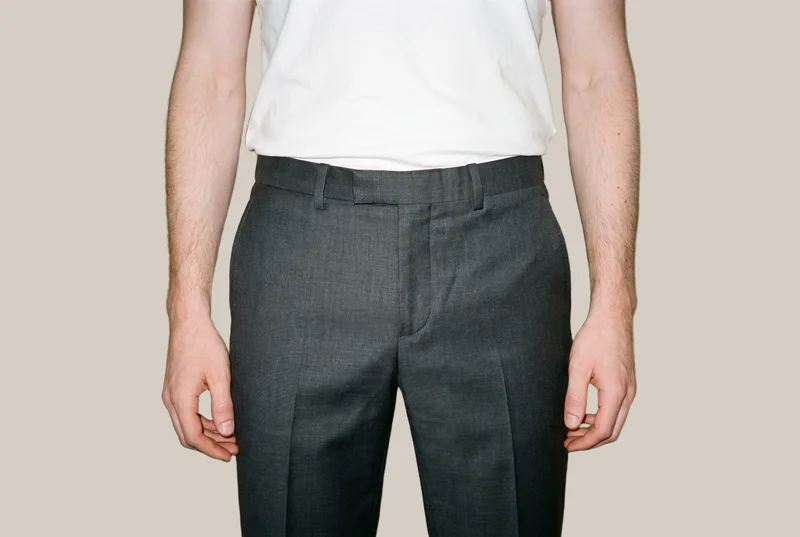 Men's charcoal suit trousers shown from the front, framed from the hips with the hips level. The trousers are presented against a flat London Fog backdrop.