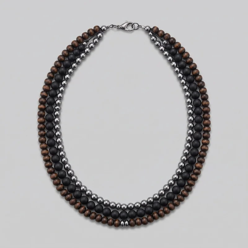 A complete multi-strand beaded necklace is laid flat in a U shape. Three parallel rows of round beads are visible, including a grain-patterned outer row, a smooth matte center row, and a reflective polished inner row. Short knotted-cord connector sections, small spacer beads, jump rings, and a lobster-claw clasp are shown at the top.