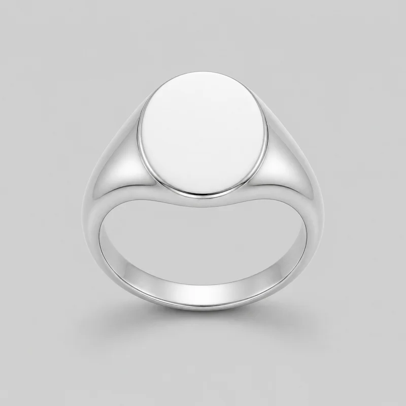 A standalone close view of a silver signet ring with a rounded continuous band, a circular flat face, and a raised rim surrounding a smooth blank center. The shoulders flare into the face with curved side panels, while the band has rounded inner and outer edges. No logos, engravings, stones, prints, or other embellishments are visible.