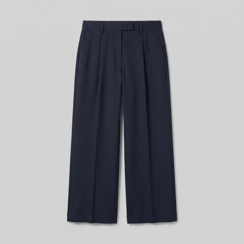 Navy tailored wide-leg trousers shown in a front flat-lay view. The full-length trousers have a high-rise waistband with belt loops and an extended tab, a concealed fly, inward front pleats, vertical pressed creases, side slash pockets, straight legs, and straight hems. No logos, prints, patches, embroidery, or embellishments are visible.