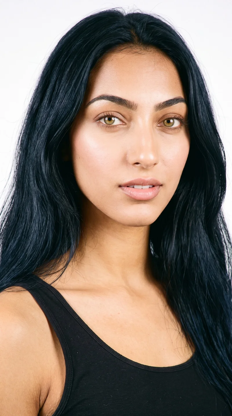 This 19-year-old Arab woman has warm honey-toned skin with a golden undertone. Her heart-shaped face has a wider forehead that narrows to a more pointed chin, framed by medium-thickness eyebrows. She has amber eyes with golden tones and full lips. Her long, deeply saturated black hair is worn loose past the shoulders with natural volume.