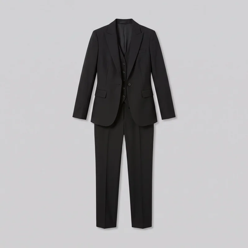 A standalone front view shows a women's black three-piece tailored suit with a structured single-breasted blazer, matching button-front waistcoat, and straight-leg trousers. The blazer has sharp shoulders, notched lapels, a curved front hem, one visible front button, a welt chest pocket, two lower flap pockets, front darts, and panel seams. The waistcoat has a V-shaped neckline and vertical button row, while the trousers have pressed front creases and plain full-length hems.