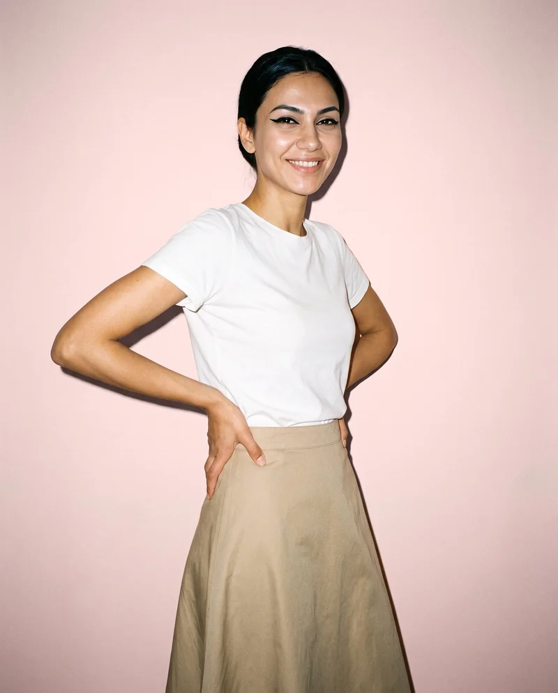 A 22-year-old Turkish woman models a khaki cotton maxi skirt in a three-quarter-length, angled-front view with her hands on her hips and a natural expression. The skirt is shown against a Misty Rose studio-wall backdrop.