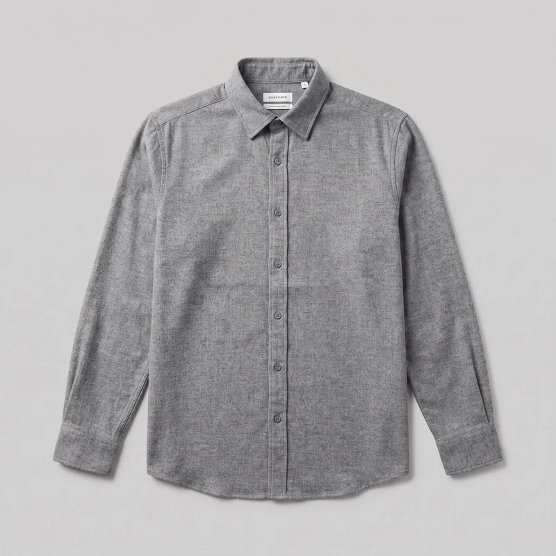 A grey brushed flannel long-sleeve button-up shirt is shown in a mostly complete front flat-lay view as a standalone garment. It has a pointed fold-down collar, a full center-front button placket, visible yoke and shoulder seams, button cuffs with sleeve plackets, and a slightly curved shirt-tail hem. The fabric has a fine heathered, speckled texture, with no visible chest pockets, logos, prints, patches, embroidery, or embellishments.