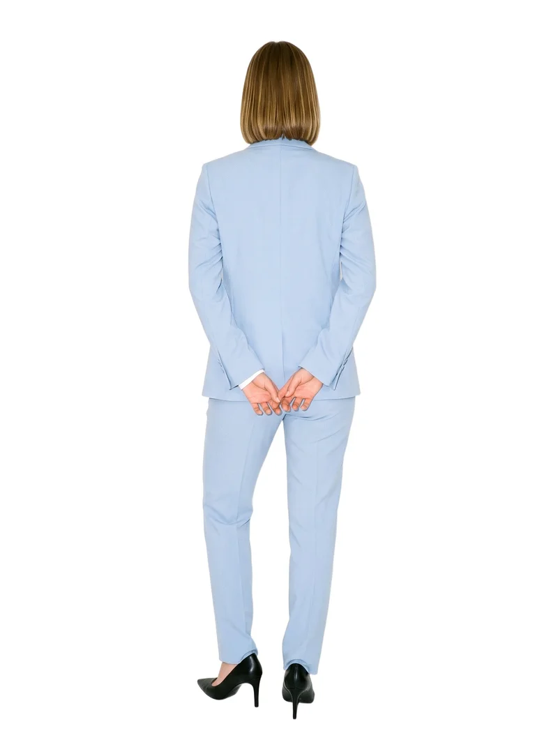A 24-year-old Caucasian woman wears a powder blue trouser suit in a full-body rear view, standing with her hands behind her back. The suit is shown against a pure white backdrop.