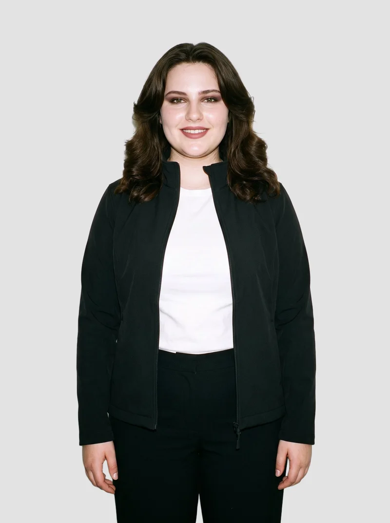 An 18-year-old Caucasian woman stands straight in a front-facing three-quarter-length view, wearing a women's black softshell jacket and smiling. A flat Fog Grey backdrop frames the studio-cutout composition.