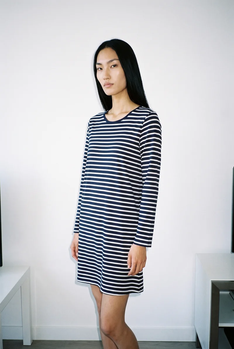 A 21-year-old Korean woman wears a striped nightdress in a three-quarter-length view. She stands in a relaxed pose facing the camera from a front three-quarter angle with a soft expression. A minimalist apartment serves as the backdrop.