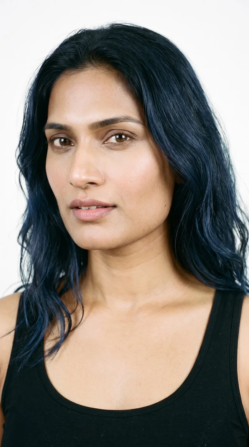 A 35-year-old Indian woman with medium skin and an olive-green undertone. Her square face has a broad forehead and a strong, defined jaw, creating an angular, structured appearance. She has medium-thickness eyebrows, medium lips, and brown eyes. Her black hair is styled in loose, slightly tousled waves with natural volume.