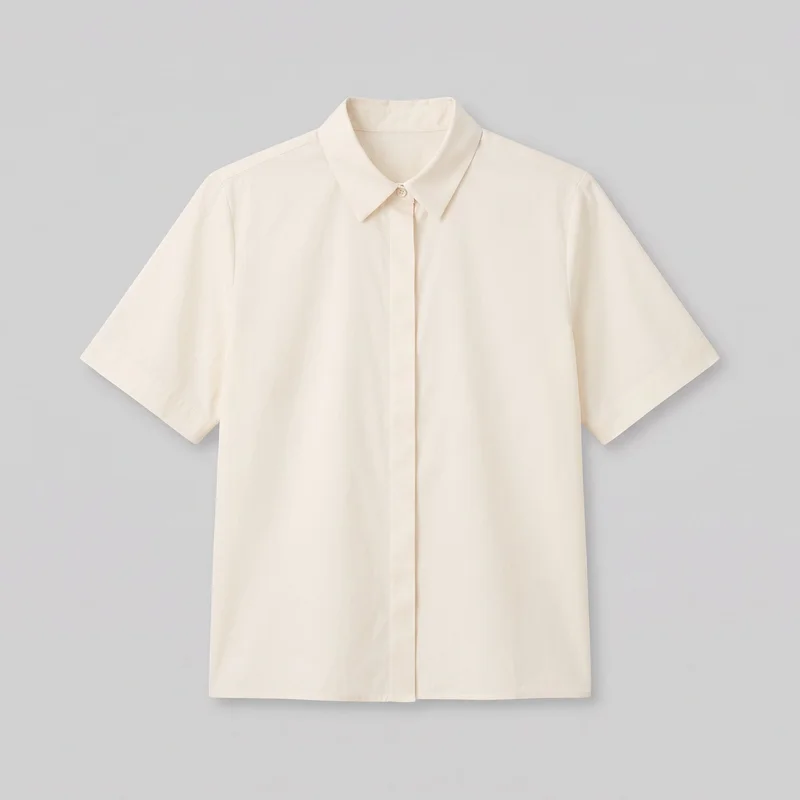 A cream cotton short-sleeve button-up blouse is shown alone from the front, with its full outline visible. It has a regular straight silhouette, a pointed fold-over collar on a collar stand, set-in shoulders, short straight sleeves, and a straight bottom hem. The centered concealed button placket has one exposed button at the collar, with visible shoulder seams and no visible chest pockets, logos, prints, patches, embroidery, or embellishments.