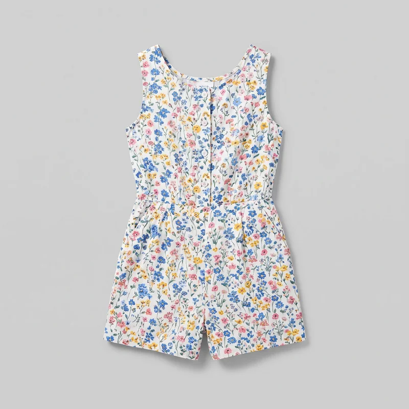 A complete front view of a sleeveless short romper with a rounded scoop neckline, wide shoulder coverage, deep armholes, and a straight button-front bodice. Vertical seams, a defined waist seam with light gathering, relaxed shorts, straight hems, and a center front leg split are visible beneath the all-over small-scale wildflower stem print.