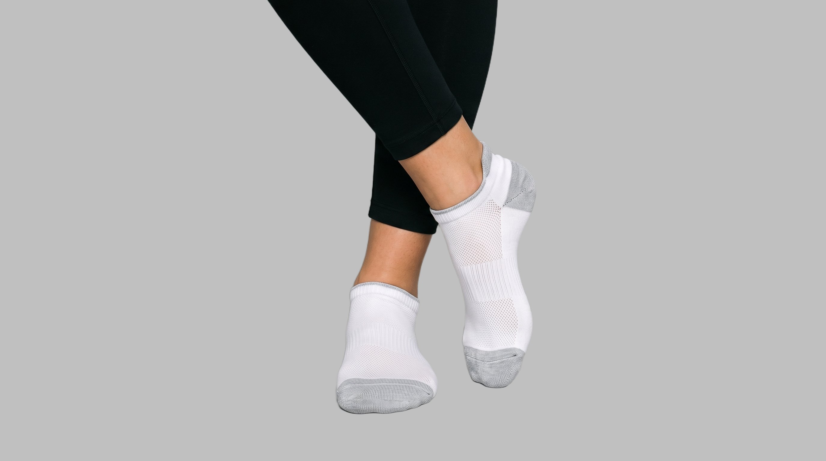 Both feet are shown from the front with the ankles crossed, wearing women's ankle sports socks. A flat Silver Mist backdrop surrounds the studio-cutout view.