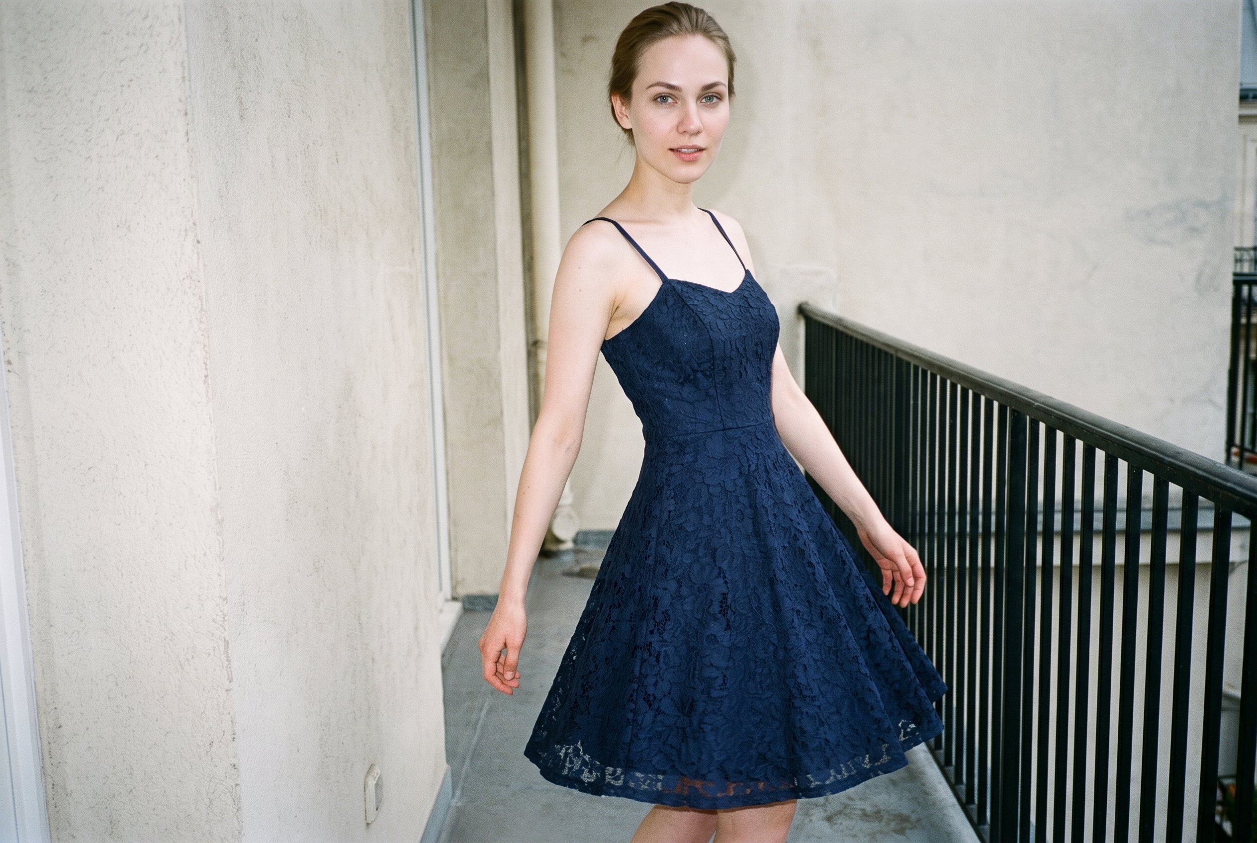 A 22-year-old Slavic woman wears a navy lace cocktail dress in a three-quarter-length, angled-front view as she walks with a confident expression. A Paris balcony forms the backdrop.
