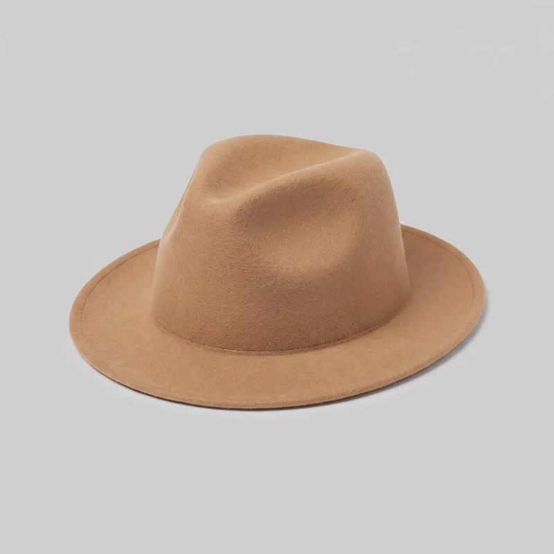 A standalone angled view shows a full camel felt fedora with a structured crown, lengthwise top crease, and pinched side dents at the front. The crown sits directly on a continuous, slightly curved molded brim, with visible stitching around the crown base and near the outer brim edge. No hat band, logo, print, embroidery, fastener, or other embellishment is visible.