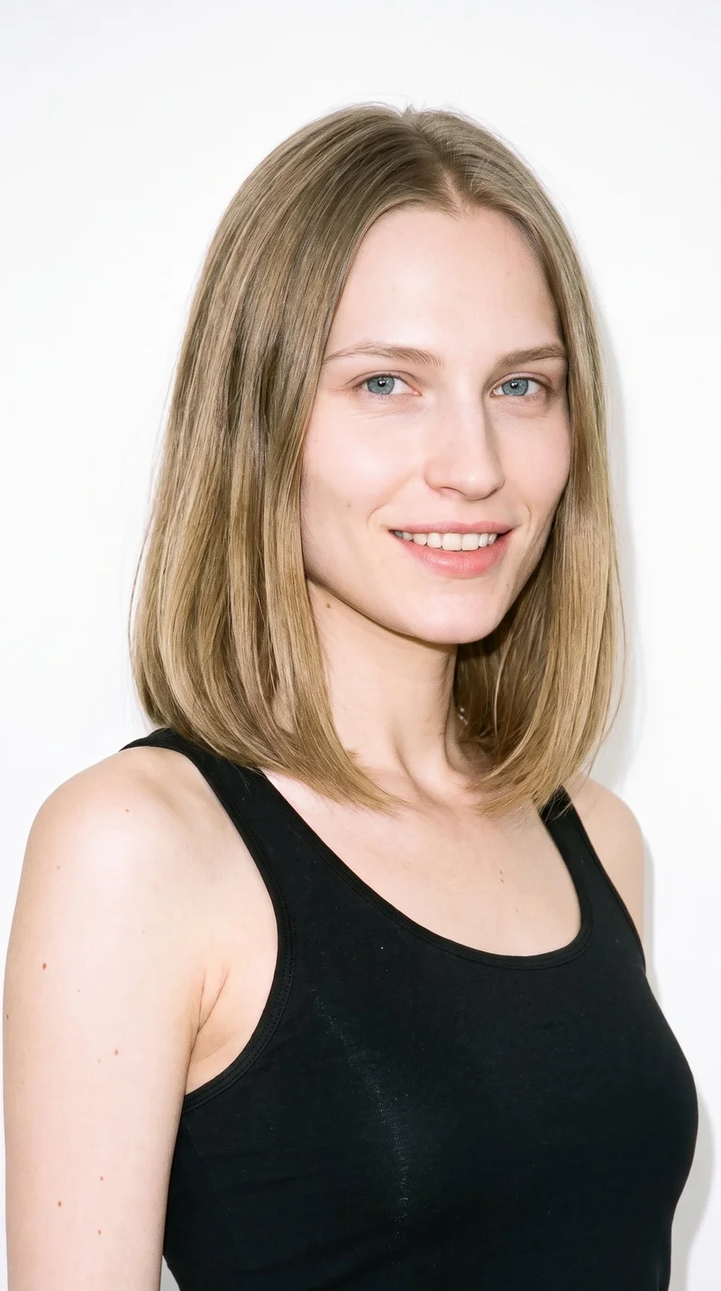 This 27-year-old Slavic woman has pale skin with a neutral undertone and a triangle-shaped face, with a wide jaw that narrows toward the forehead. She has thin eyebrows, blue eyes with a cool undertone, and full lips. Her dark-blonde hair is styled in a long bob falling between the chin and shoulders.