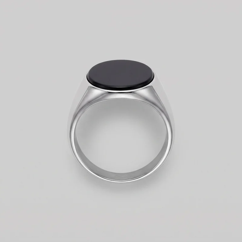 A standalone onyx signet ring is shown with its circular band opening, rounded shank, and smooth polished surfaces. Sloped shoulder panels expand into a raised oval flat face, with a defined rim around the top inset.