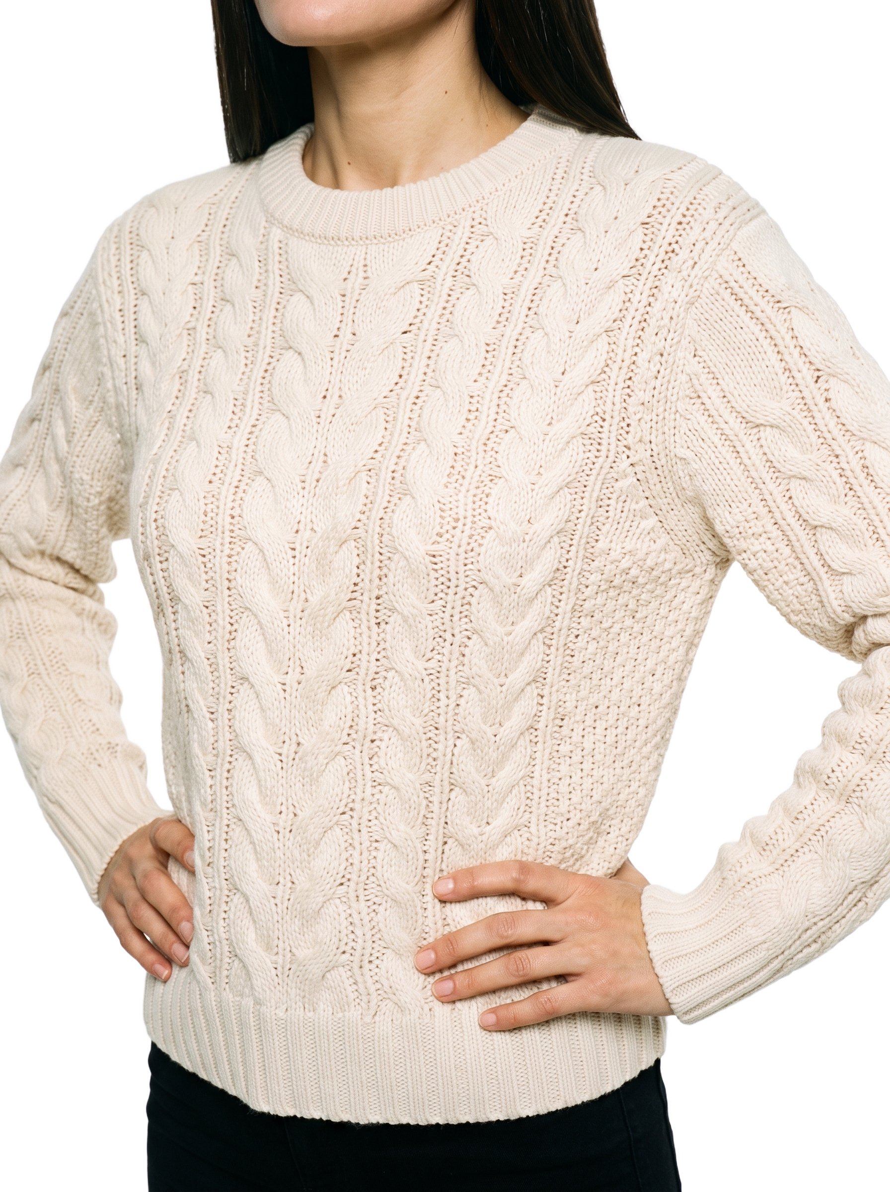 A woman is shown from the torso in an angled front view, wearing a cream cable-knit pullover jumper with her hands on her hips. The garment is presented against a pure white backdrop.
