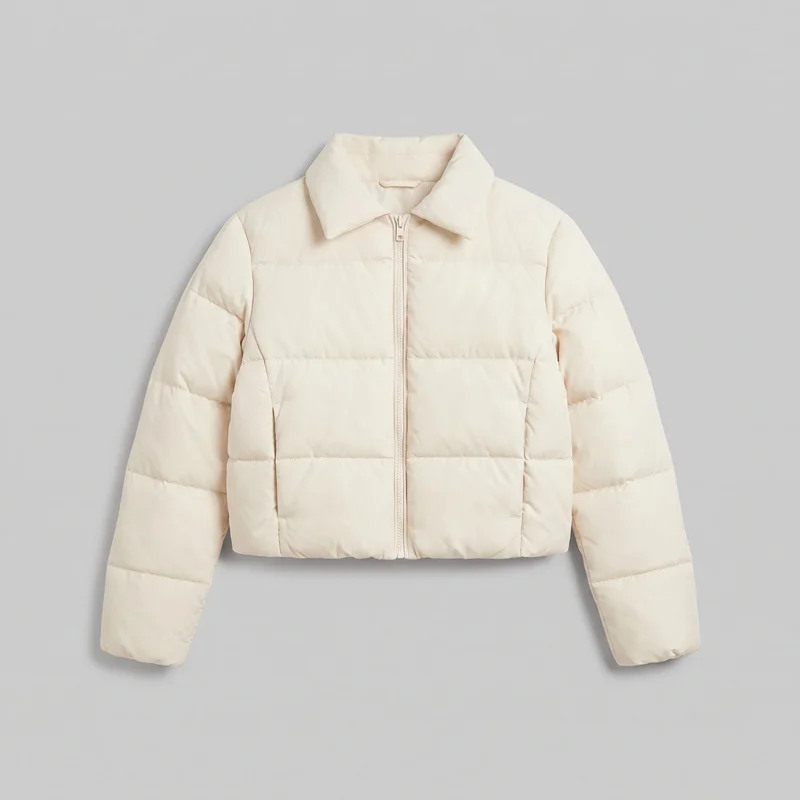A cream cropped puffer jacket shown alone in a front view. It has a boxy relaxed silhouette, a fold-down pointed collar, long sleeves, a straight cropped hem, a full-length center zipper, horizontal quilted baffles, vertical panel seams, and two lower-front vertical welt pockets. The jacket has no visible logos, prints, patches, embroidery, or embellishments.