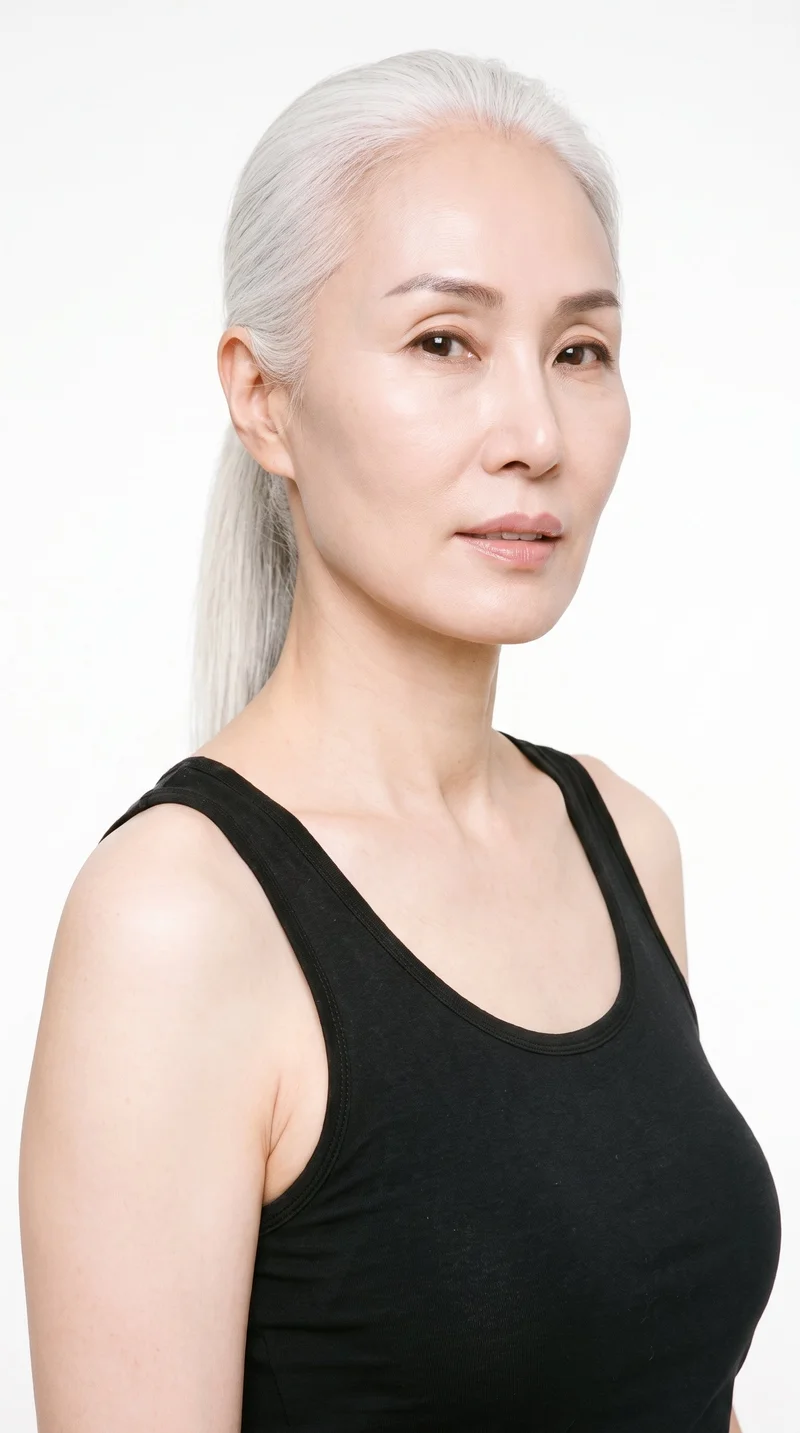 A 56-year-old Korean woman with light porcelain skin and a cool undertone. She has an elongated face with refined features and high cheekbones, medium-thickness eyebrows, brown eyes, and full lips. Her white hair is tied back into a single falling ponytail.