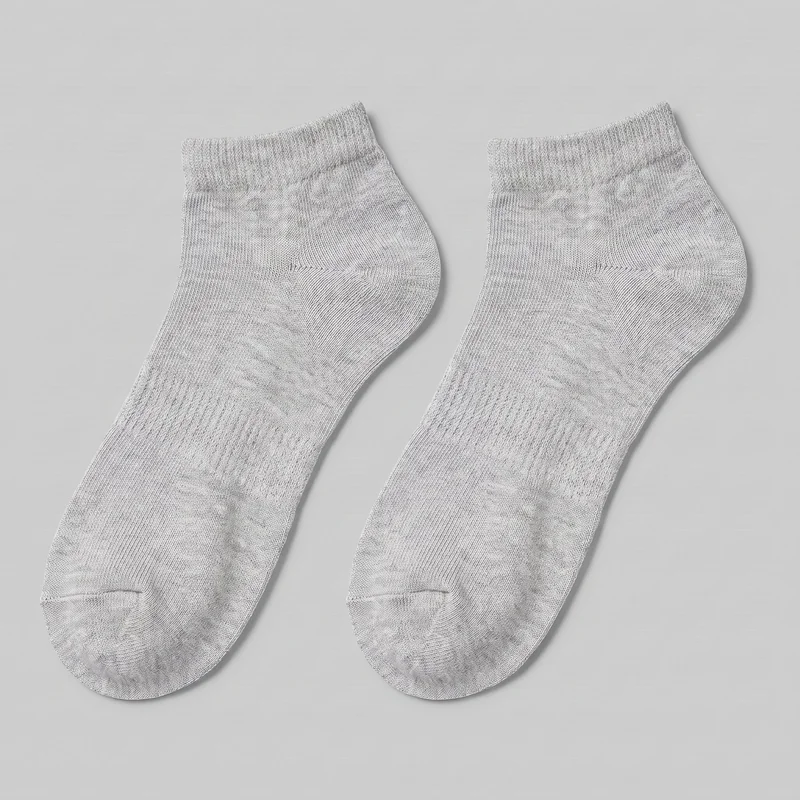 A complete pair of grey low-cut cotton ankle socks is laid flat and shown from above. The socks have rounded closed toes, visible toe seams, smooth knit foot bodies, shaped heel pockets, and short denser ribbed cuffs at the openings above the heel area. No logos, prints, patches, embroidery, or embellishments are visible.