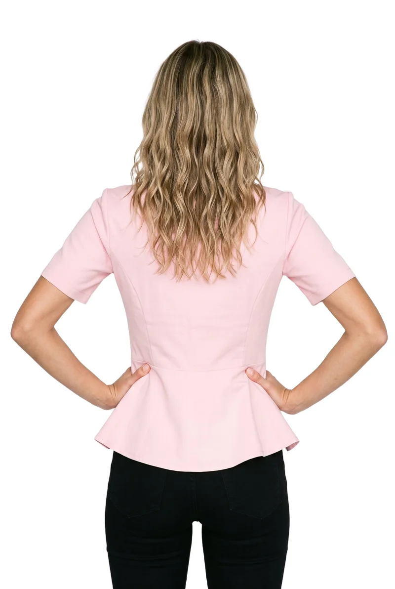 A 19-year-old Caucasian female model wears a blush pink peplum top in an upper-body rear view, standing with her hands on her hips. The garment is shown against a pure white backdrop.
