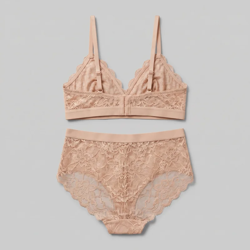 A matching nude two-piece lingerie set is arranged in a flat lay, with the bralette positioned above the high-waist brief. The bralette is shown from its back or inner side, with adjustable shoulder straps and a visible hook-and-eye closure. The high-rise brief has a floral lace body, wide waistband, and scalloped leg openings.