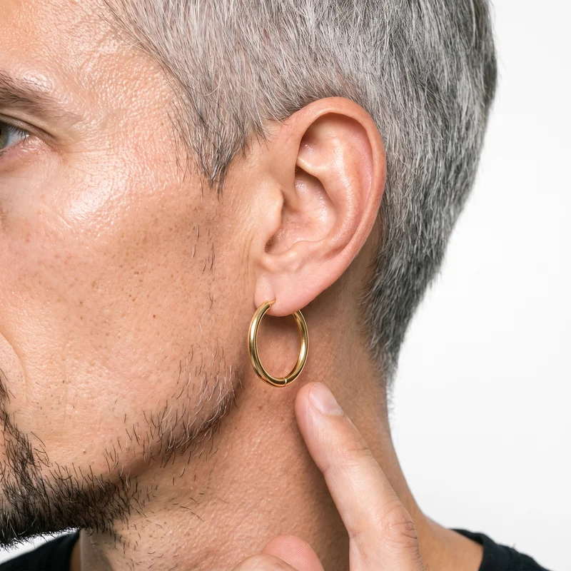 A male ear shown in side view with a finger touching the earlobe and a gold hoop earring visible against a pure white studio backdrop.