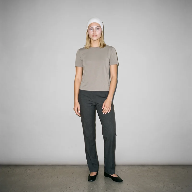 A 20-year-old Caucasian woman wears a white modal underscarf in a full-body front view, standing with her hands in front and a natural expression. A dove grey studio-wall backdrop fills the background.