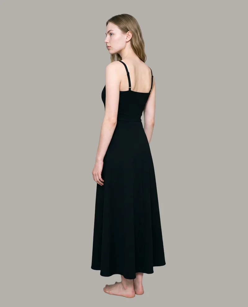 An 18-year-old Caucasian woman stands straight in a full-body, angled rear view wearing a black evening gown. The garment is shown against a flat Couture Grey backdrop.
