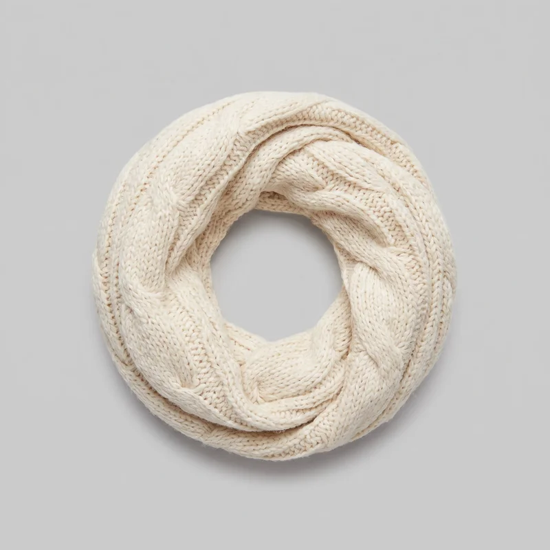 A cream tubular infinity scarf is shown laid flat and coiled into a complete ring. Alternating raised cable-braid panels and flatter ribbed knit bands run lengthwise around the loop, which has softly voluminous rolled folded edges and no visible fringe or closures.