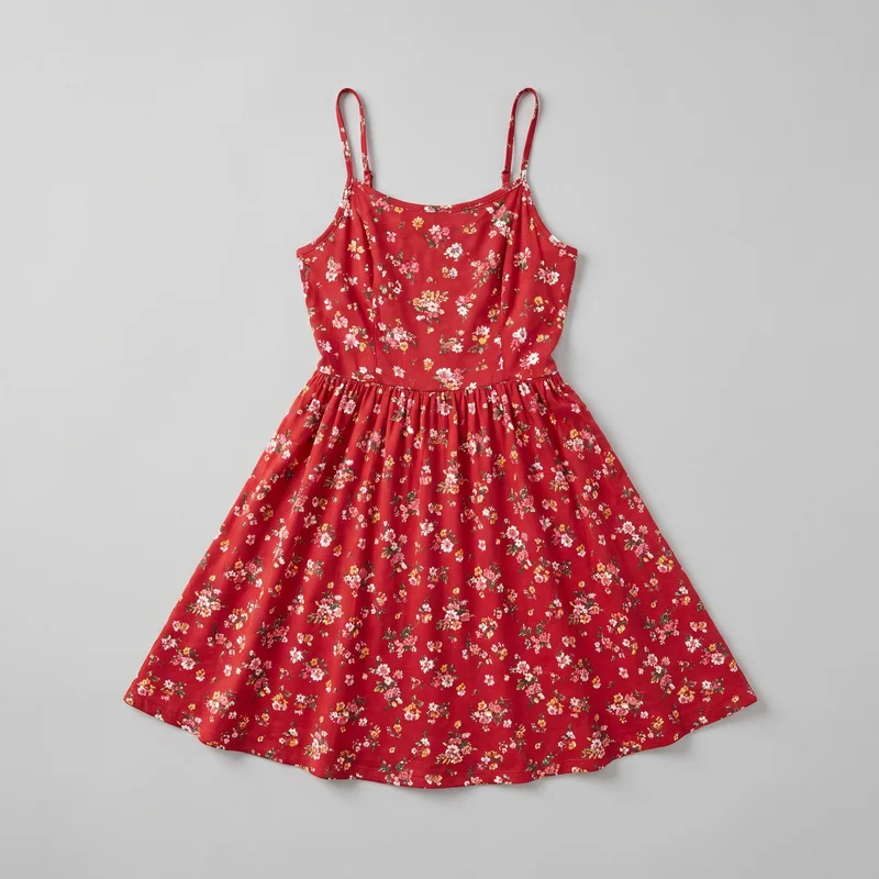 A red women's sleeveless sundress is shown in a flat-lay view. It has narrow spaghetti straps, a shallow scoop neckline, a fitted bodice with vertical panel seams, a defined waist seam, and a gathered skirt that flares into an A-line shape. The dress features an all-over small floral print with scattered blossom clusters and leafy sprigs, ending in a softly curved hem.