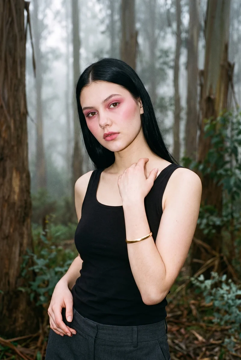 A 19-year-old Caucasian woman is shown in an upper-body, angled-front view, smiling with one hand at her collarbone to display a gold bangle. An Eucalyptus Fog Park Grove backdrop is visible.