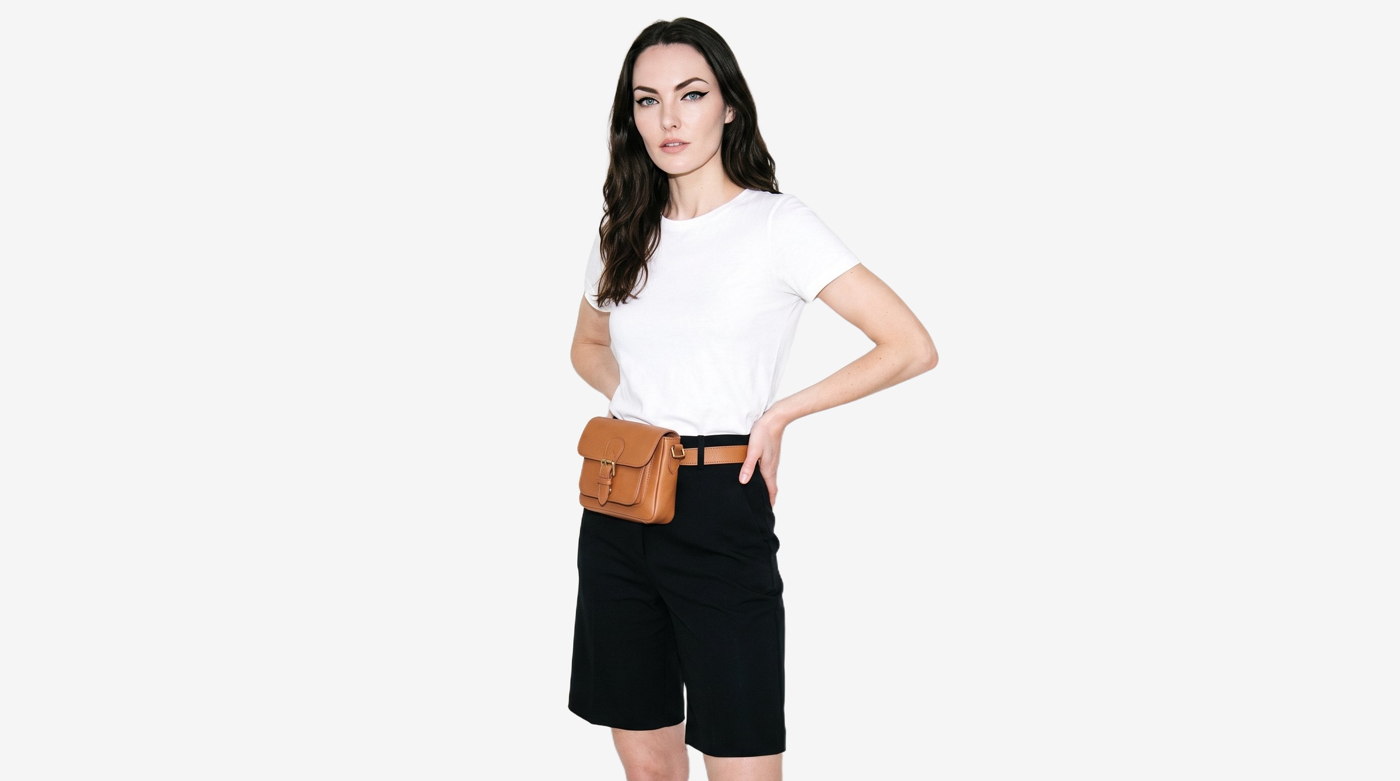 A 25-year-old Caucasian woman wears a tan leather belt bag, shown in a three-quarter-length angled front view with her hands on her hips and a neutral expression. The bag is presented against a flat cloud-white backdrop.