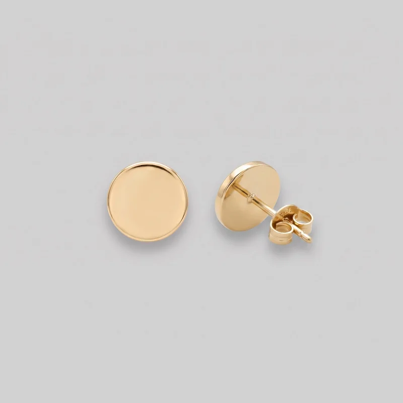 A pair of gold circular disc stud earrings is shown as a standalone product. One earring faces forward, displaying its smooth, slightly convex round front and raised rounded rim, while the other is angled to reveal its straight post and butterfly push-back clutch.