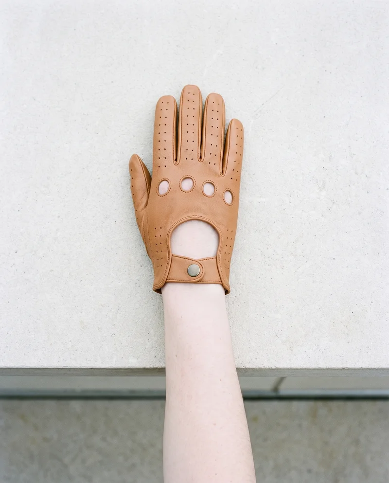 A top view shows a hand and wrist wearing women's tan driving gloves, with the hand held flat. The Penthouse Terrace serves as the backdrop.