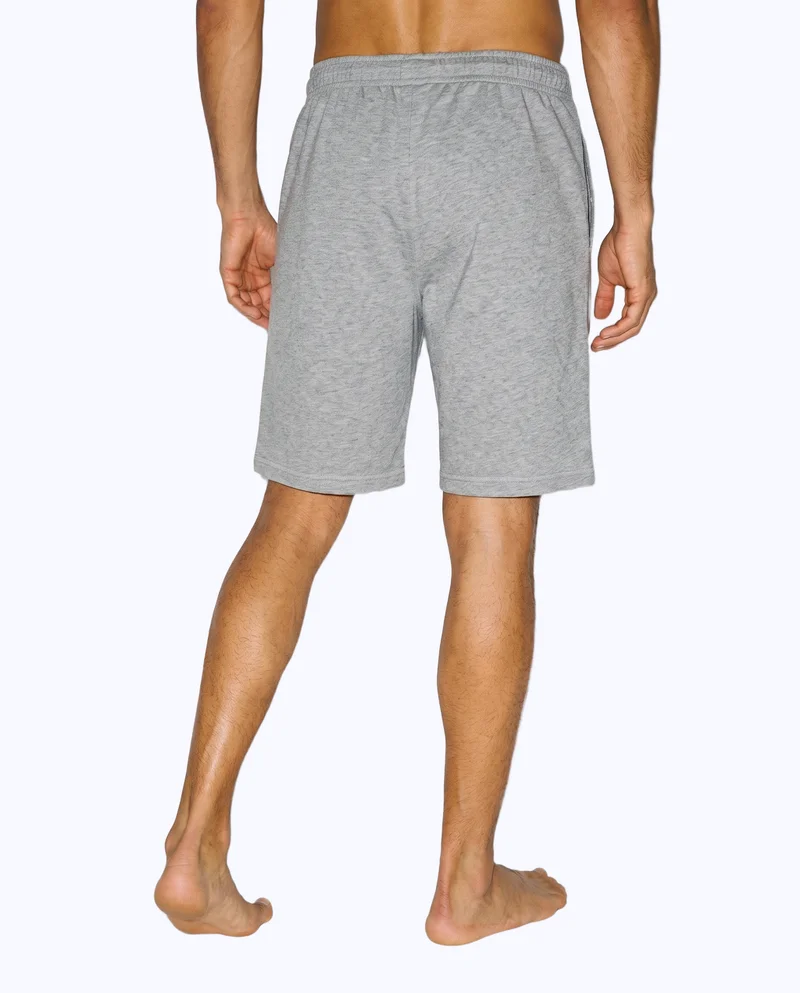 Men's grey jersey shorts shown from the back in a lower-body view, with one foot positioned forward. The shorts are presented against a flat porcelain-colored backdrop.