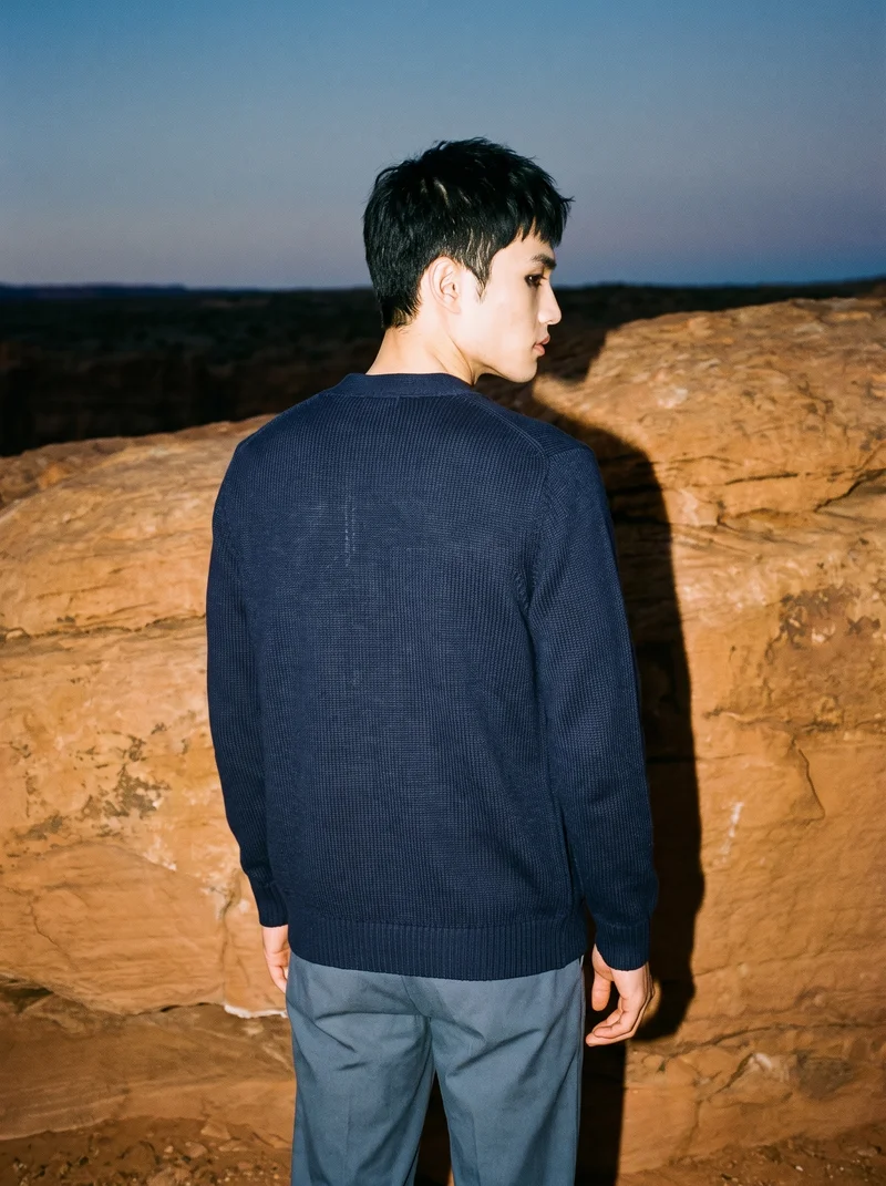 A 24-year-old Chinese man wears a men's navy wool cardigan in a three-quarter-length back view, posed with a waist twist. The Grand Canyon Rim appears as the backdrop.