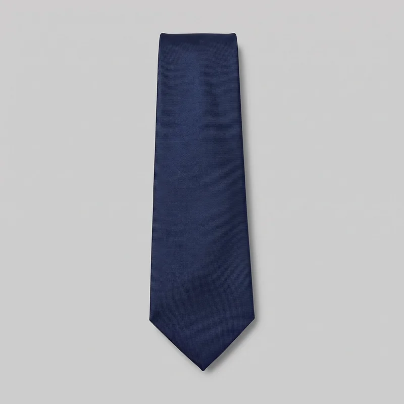 A single navy silk necktie lies flat as a standalone product. Its long tapered blade widens gradually toward a sharp V-shaped pointed lower tip and narrows toward a folded upper neck end. The tie has crisp straight side edges and a solid fine-woven surface, with no visible knot, hardware, logo, print, or embellishment.