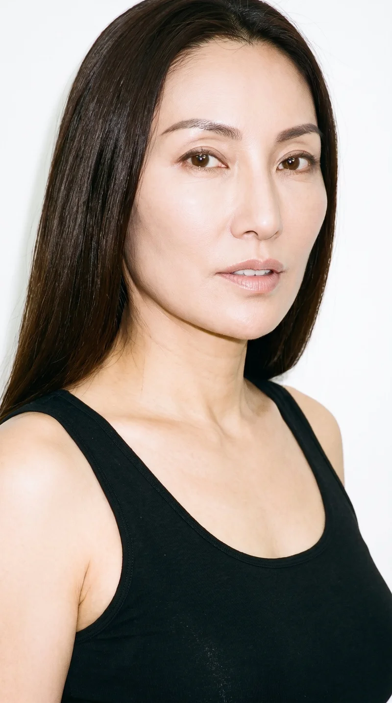 A 49-year-old Chinese woman with a light porcelain skin tone and neutral undertone has an elongated, refined face with high cheekbones. Her medium-thickness eyebrows frame very dark, near-black eyes, and she has medium lips. Her long dark-brown hair falls straight without waves or layers.