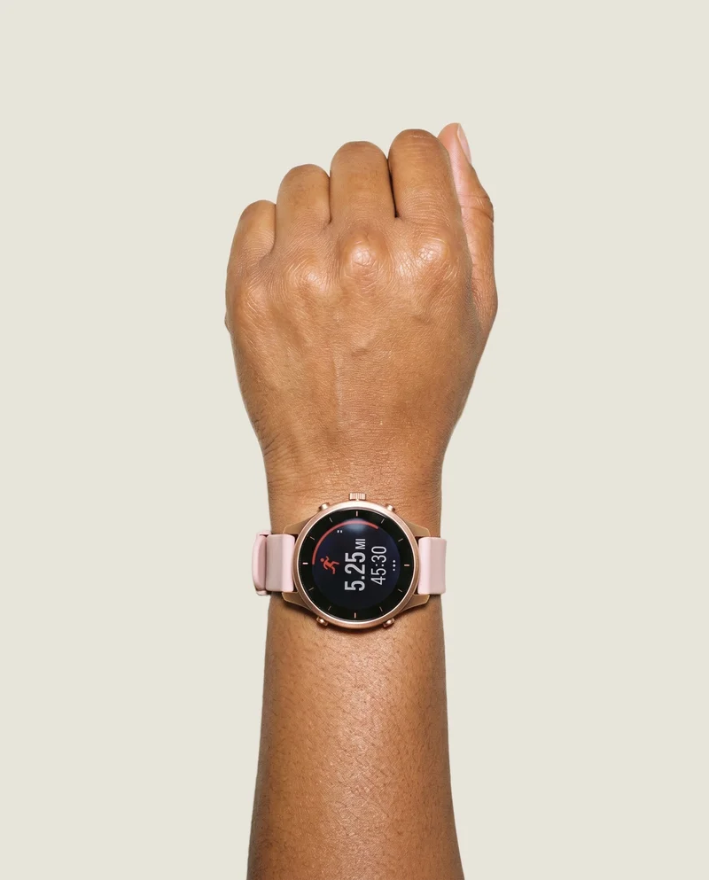 A women's GPS sports watch is worn on a closed hand and wrist, shown from a top view. The hand and wrist are the only visible body area, framed against an Oyster Pearl flat-color backdrop.