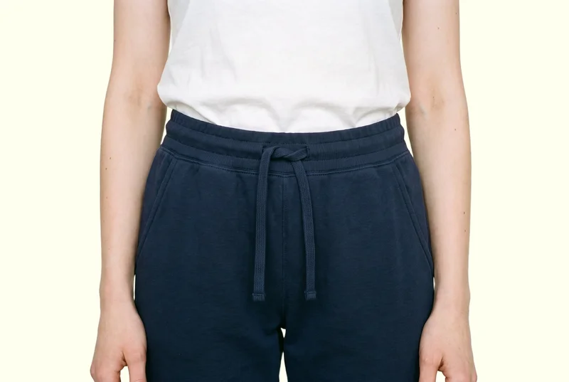 Women's navy cotton joggers shown from the front, framed from the hips with the hips level. The garment is presented against an ivory lace backdrop.