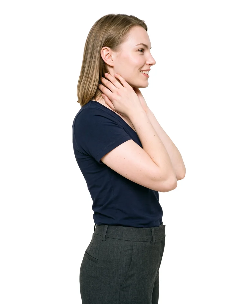 A 23-year-old Caucasian woman wears a navy V-neck T-shirt in an upper-body side-view composition. Her hands are on her neck, and she is smiling against a pure white backdrop.