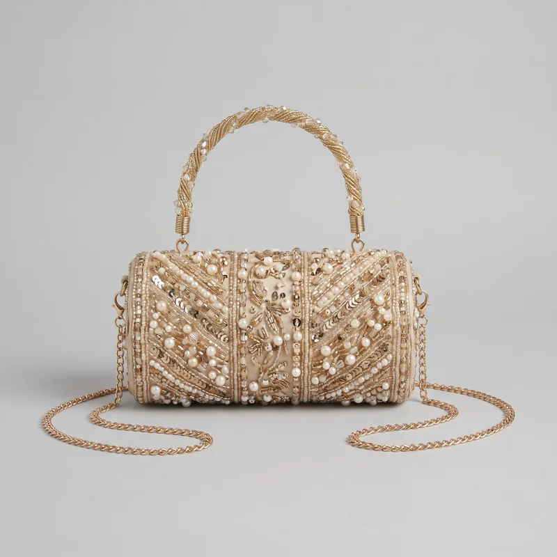 A structured barrel-shaped evening clutch with a flat top panel, rounded end panels, and an arched top handle. Its front is divided by raised vertical bands and bordered seams, with dense bead, tube-bead, sequin, and pearl-like ornamentation arranged in diagonal chevrons, radiating panel motifs, and scattered raised accents. A chain shoulder strap attaches at visible side rings, while the cord-wrapped handle has faceted bead accents, coiled collars, and loop hardware.
