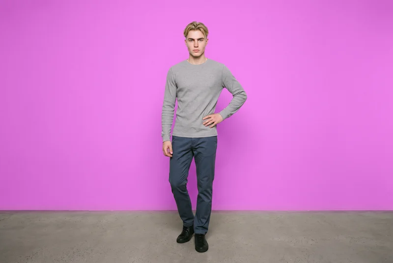 A 19-year-old Caucasian male model wears a men's grey thermal base layer in a front-view environmental composition. He stands with his weight back and a neutral facial expression against an Orchid studio-wall backdrop.